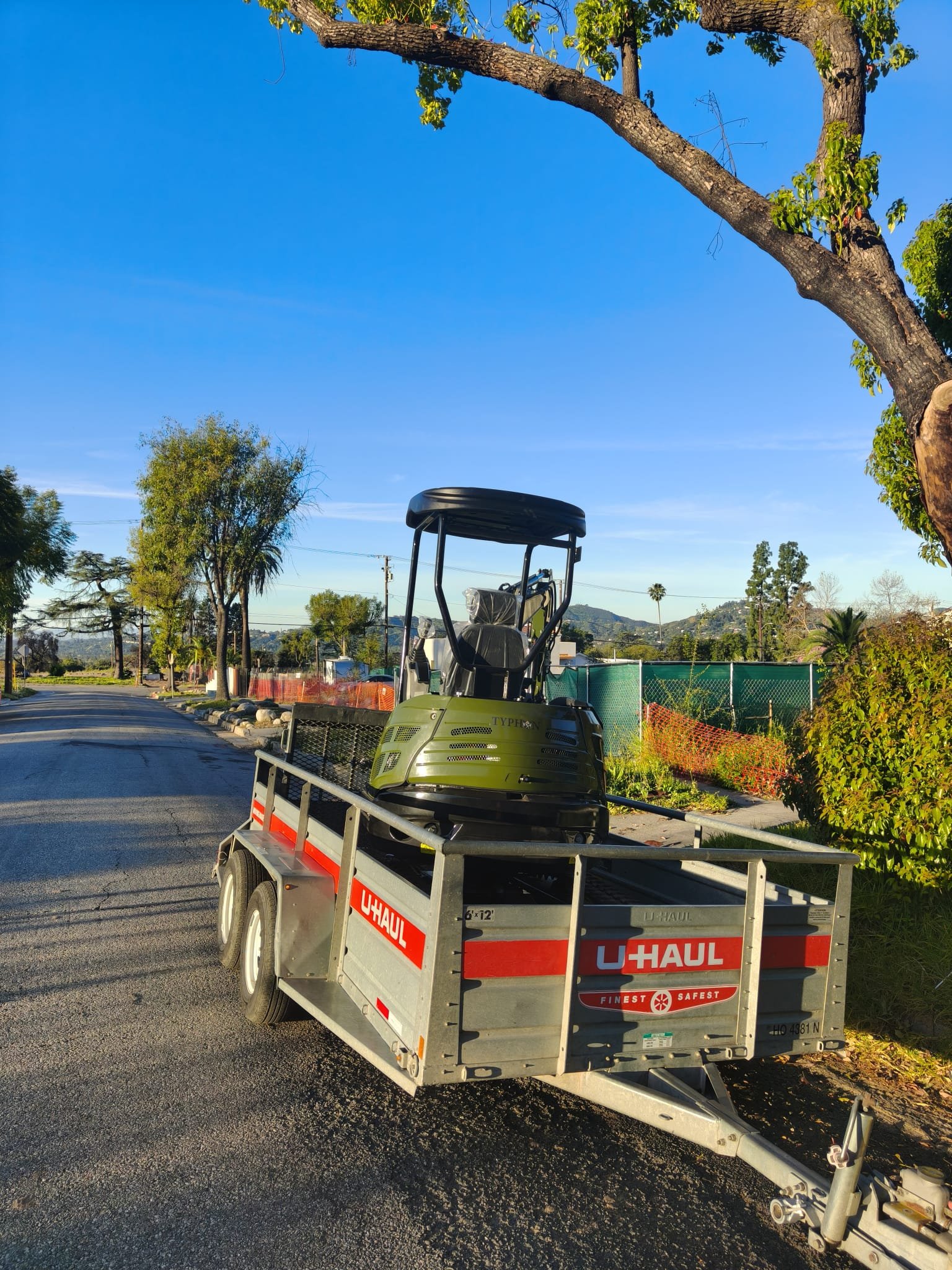 Green TYPHON mini excavator loaded onto a rental trailer